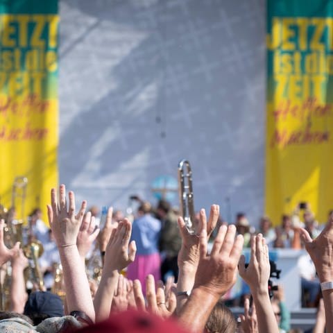 Musiker*innen beim Evangelischen Kirchentag in Nürnberg halten vor einer Bühne ihre Hände und ihre Instrumente in die Höhe