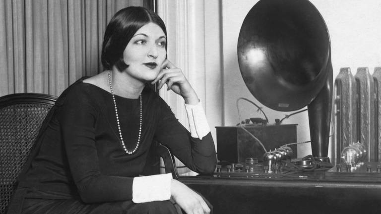 Schwarz-weiß: Frau mit Perlenkette und 1920er Frisur hört Radio