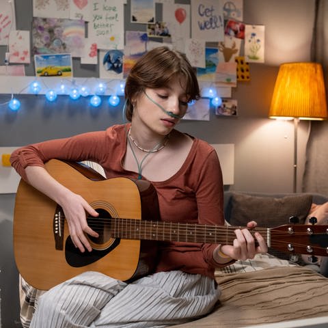Symbolbild: Eine Teenagerin musiziert in einem Krankenhausbett