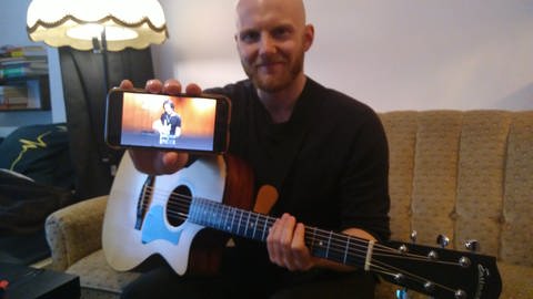 Leif Jensen mit Gitarre - hält ein Smartphone in die Kamera. (Foto: Valentin Stötzer)