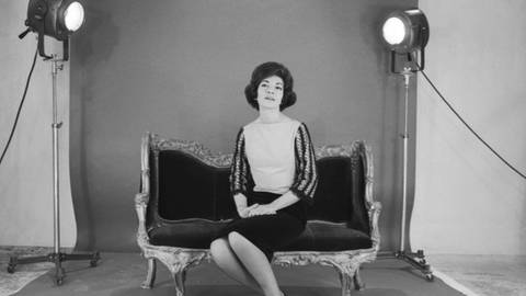 Maria Callas sitzt auf einem Sofa und wird von beiden Seiten von Scheinwerfern angeleuchtet