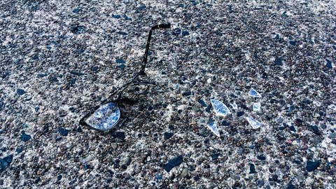 Eine zerbrochene Brille liegt mit Glassplittern auf der Straße. (Foto: IMAGO, IMAGO / Shotshop)