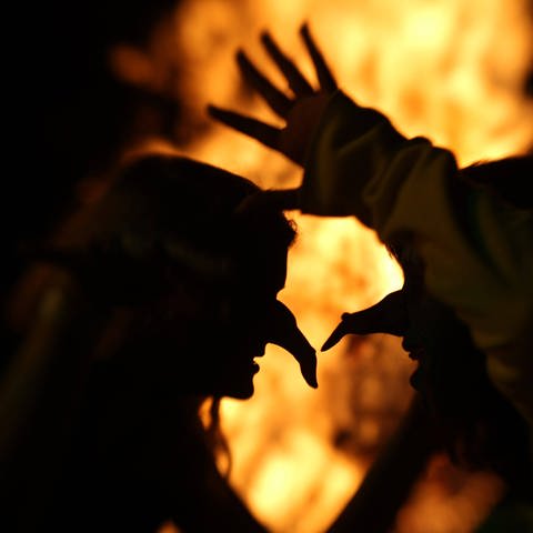 Als Hexen verkleidete Personen tanzen in der Walpurgisnacht vor einem Feuer