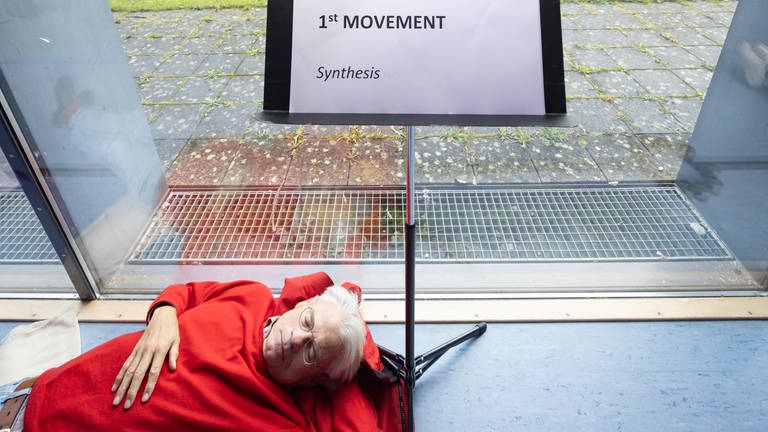 Mann liegt mit geschlossenen Augen am Fuße eines Notenständers (Foto: SWR, Ralf Brunner)