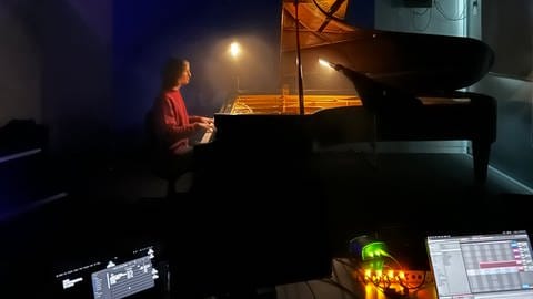 Mann sitz fast im Dunklen am Klavier, die Tastaturbeleuchtung und das Interface zur Lichtsteuerung im Vordergrund leuchten am Hellsten