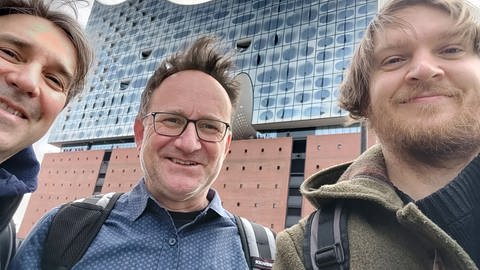Drei Männer stehen vor der Elbphilharmonie Hamburg