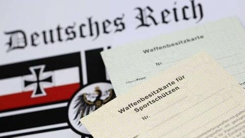 Zwei Waffenbesitzkarten vor einer Fahne des Deutschen Reiches und dem Schriftzug Deutsches Reich. (Foto: IMAGO, Imago/Fotograf XY - xWuest/Eibner-Pressefotox)