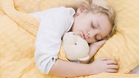 Ein Kind mit Stofftier schläft im Bett
