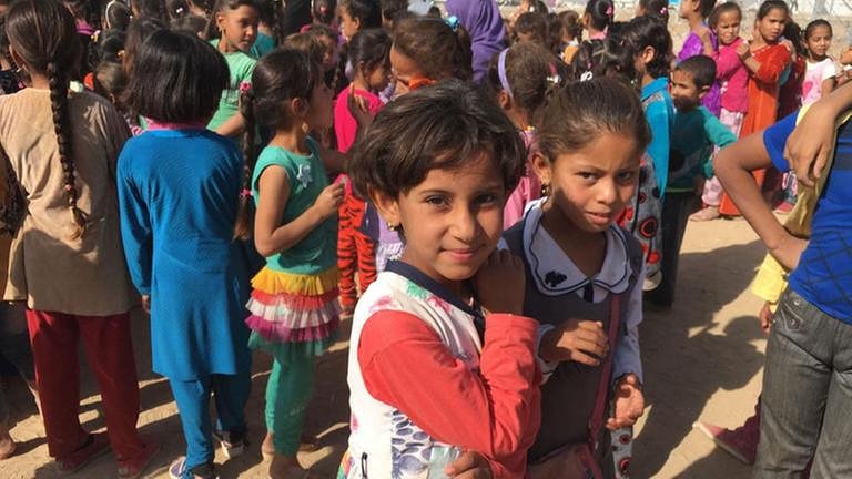 Eine große Kindergruppe im Flüchtlingslager. Zwei Mädchen gucken fragend in die Kamera. (Foto: SWR, SWR - Anna Osius)