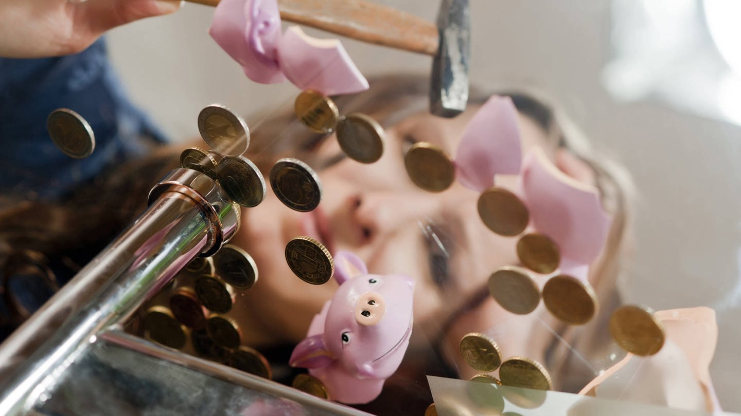 Eine frau schaut auf ein zerschlagenes Sparschwein, das nicht viel Geld in sich hatte (Foto: IMAGO, IMAGO / blickwinkel)