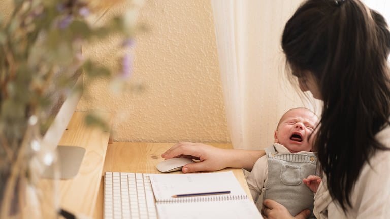 Eine Frau arbeitet am Computer und hat dabei ihr Baby auf dem Arm