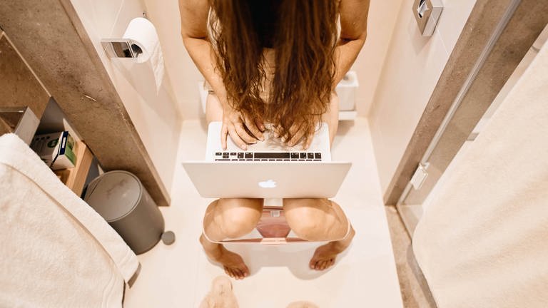 Eine Frau sitzt auf der Toilette und bedient dabei noch ihren Laptop