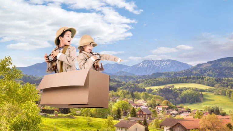 Kinder in fliegendem Karton über einem Alpendorf