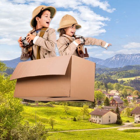 Kinder in fliegendem Karton über einem Alpendorf