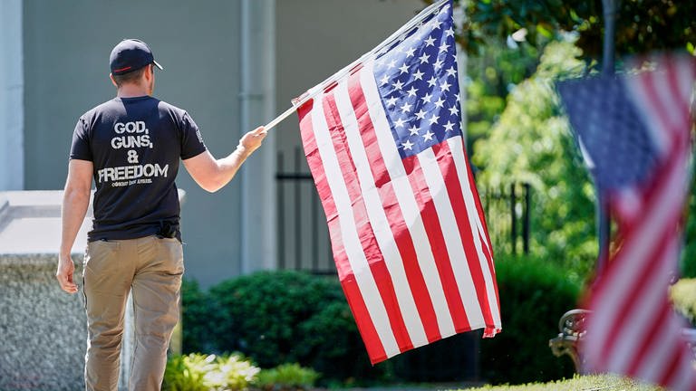 God, Guns & Freedom: Ein Mann mit der US-Flagge bei Protesten am 2. Mai 2020 in Morganton  North Caroline. Gut 50 Menschen forderten den Gouverneur von North Carolina, Roy Cooper, auf, die Beschränkungen, die wegen der COVID-19-Pandemie verhängt worden waren, zu lockern.  (Foto: IMAGO, imago images / ZUMA Wire)