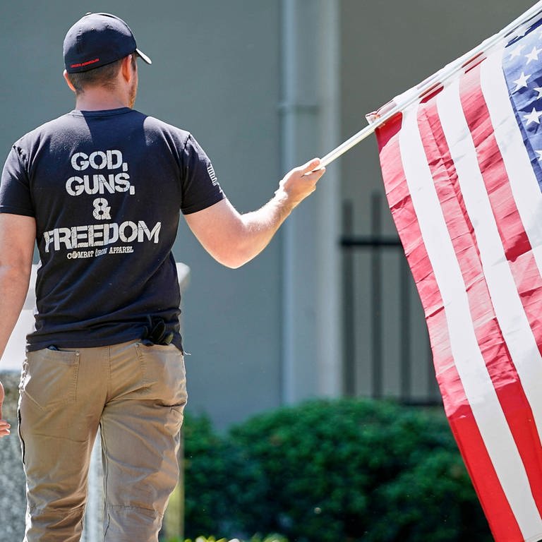 God, Guns & Freedom: Ein Mann mit der US-Flagge bei Protesten am 2. Mai 2020 in Morganton  North Caroline. Gut 50 Menschen forderten den Gouverneur von North Carolina, Roy Cooper, auf, die Beschränkungen, die wegen der COVID-19-Pandemie verhängt worden waren, zu lockern. 
