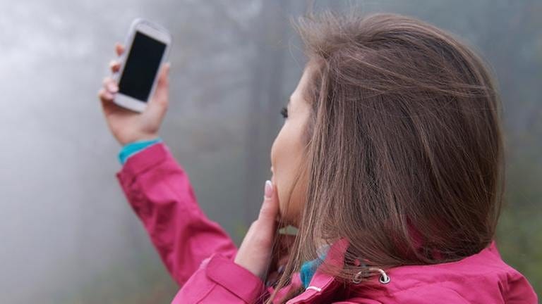 Eine Frau sucht mit ihrem Handy nach einem Signal (Foto: Getty Images, Thinkstock -)