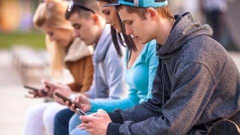Jugendliche sitzen mit ihrem Handy auf einer Bank