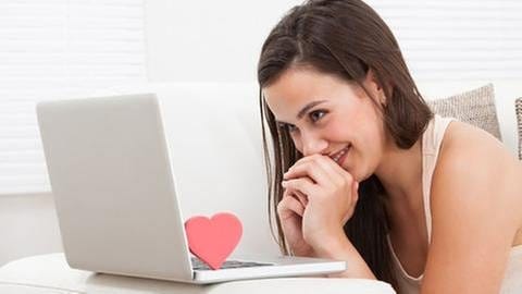 Eine junge Frau sitzt vor einem Laptop und sieht verliebt in den Monitor (Foto: Getty Images, Thinkstock -)