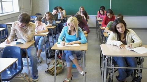 Schüler schreiben eine Prüfung und dahinter befindet sich ein Tafel. (Foto: Getty Images, Thinkstock -)
