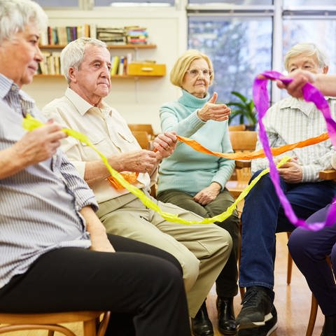 Senioren mit Demenz machen eine Übung mit bunten Stoffbändern für Interaktion (Foto: picture-alliance / Reportdienste, picture alliance / Zoonar | Robert Kneschke)