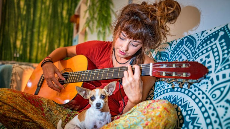 Eine junge Frau spielt Gitarre: Musikwissenschaftlerinnen und Hirnforscher versuchen in der Musik Merkmale zu identifizieren, die bei allen Menschen eines Kulturkreises oder sogar weltweit dieselben Gefühle auslösen (Foto: IMAGO, IMAGO / Westend61)