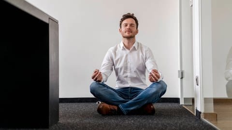Mann meditiert im Büro. Achtsamkeitstrainings sollen die innere Einstellung zur Arbeit verändern, sodass Arbeitende weniger stressanfällig sind.  (Foto: IMAGO, IMAGO / Westend61)