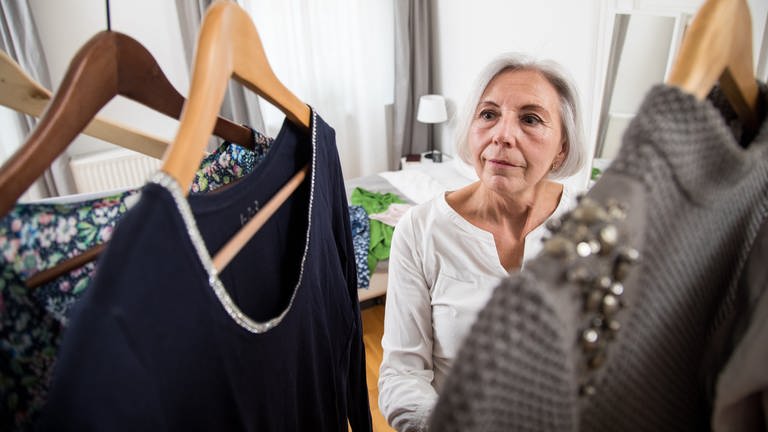 Seniorin sortiert Kleider: Döstädning ist ein Aufräum-Trend aus Schweden: aufräumen und ausmisten, um im Todesfall die Angehörigen nicht zu belasten. Und nicht nur ältere Menschen entrümpeln unter dem Vorwand „Todesputz“, auch Jüngere fangen schon damit an.