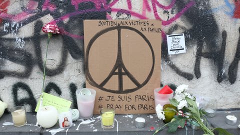 Pappschild mit einem zum Peace-Symbol stilisierten Eiffelturm inmitten von Blumen: Menschen zeigen Anteilnahme für die Opfer der Terroranschläge am 13. November 2015 in Paris: #JeSuisParis #PrayForParis