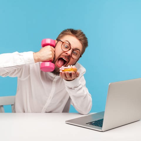 Mann am Laptop isst und "telefoniert" mit einer Hantel am Ohr: Oft heißt es in Medienberichten: Die Aufmerksamkeitsspanne schrumpft, es gelingt uns immer seltener, uns über längere Zeit zu konzentrieren, ohne uns ablenken zu lassen.