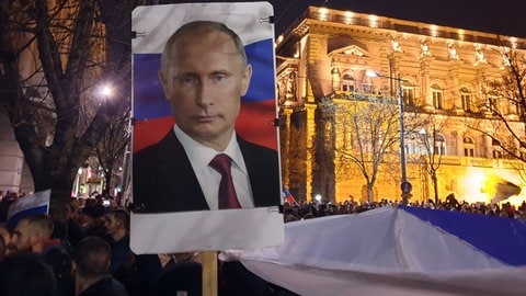 IMAGO  ITAR-TASS (Foto: IMAGO, Das Porträt des russischen Präsidenten Wladimir Putin wird während einer Kundgebung zur Unterstützung Russlands und des Donbass in Belgrad auf einem Plakat getragen. Die Demonstranten unterstützen das russische Vorgehen in der Ukraine. Nach Angaben der Organisatoren nahmen etwa 50.000 Menschen an der Veranstaltung vor der russischen Botschaft teil. In Europa gibt es Sorgen, dass sich der Konflikt zwischen Russland und der Ukraine auch auf den Balkan ausdehnen könnte.)