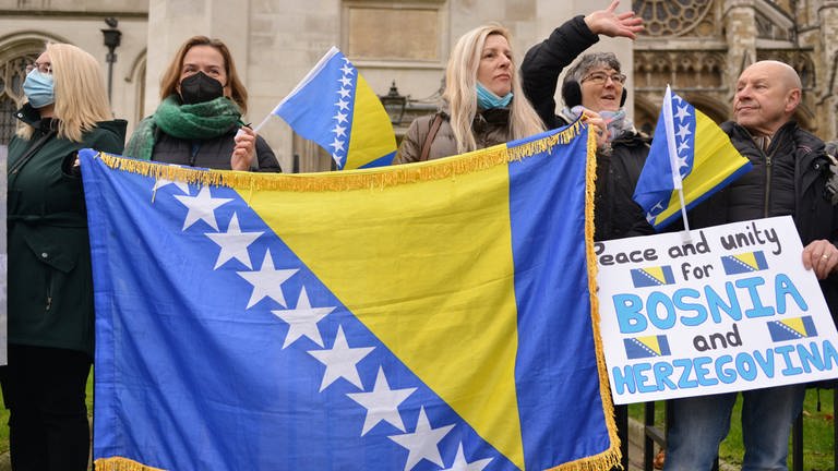 Demonstranten halten während einer Kundgebung Fahnen und Transparente hoch: Die bosnisch-herzegowinische Diaspora und Unterstützer der Einheit des Landes versammelten sich am Parliament Square in London, um das Bewusstsein für eine potenzielle neue Krise in Bosnien zu schärfen. (Foto: IMAGO, IMAGO / ZUMA Wire)