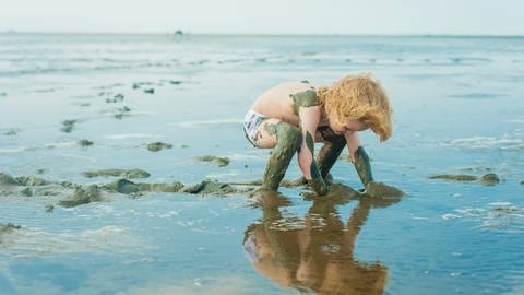 Kind spielt am Strand: Altersgerechte Erklärungen helfen Kindern, Grenzen zu verstehen und zu akzeptieren: Wenn die Flut kommt, wird es im Wattenmeer gefährlich (Foto: picture-alliance / Reportdienste, picture alliance / Westend61 | Westend61 / Jana Mänz)
