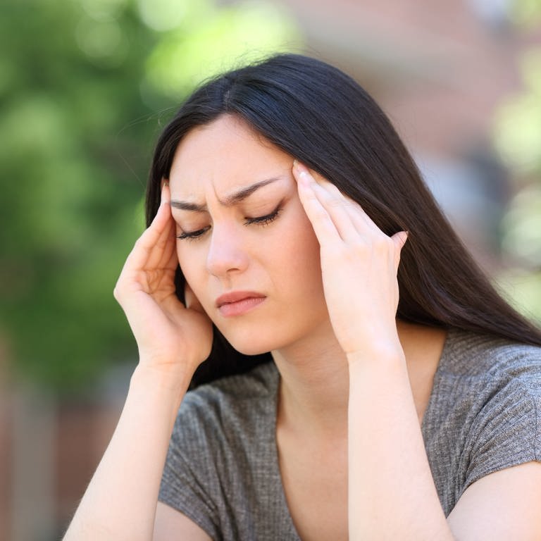Eine Frau hält sich die Hände bei geschlossenen Augen an die Schläfen vor Kopfschmerzen, Migräne. (Foto: IMAGO, IMAGO / Panthermedia)
