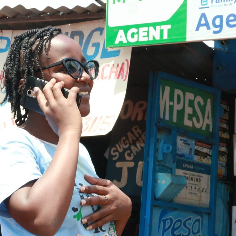 Eine Frau mit Handy am Ohr steht vor einem M-Pesa-Kiosk: Überall in Afrika zahlen Menschen per Smartphone-App. Auch Geldtransfers und andere Finanzgeschäfte werden digital erledigt. Dadurch sind Kleinhändler oder Bauern, die kein Bankkonto haben, nicht länger vom internationalen Wirtschaftssystem ausgeschlossen. Manche in Afrika entwickelte Technik wird inzwischen weltweit genutzt.  (Foto: SWR, Antje Diekhans / ARD-Studio Nairobi)