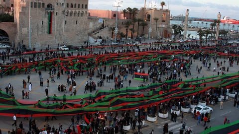 In Tripolis wird 2012 der Jahrestag der Aufstände gegen Gaddafi gefeiert. Demonstranten halten die libysche Nationalflagge in die Höhe.