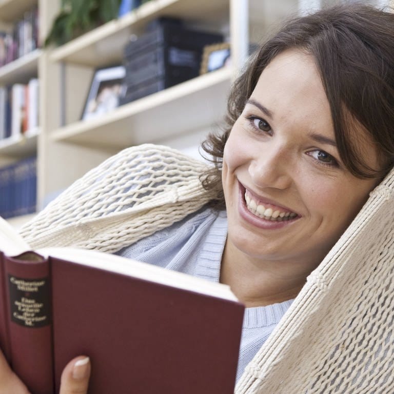 Ein Frau liest in der Hängematte: Lesen soll den Blutdruck senken, das Gehirn fit halten und sogar unser Leben verlängern. Was ist dran an diesen Thesen? (Foto: IMAGO, imago images / allOver)