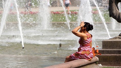 Eine Frau kühlt sich in der Sommerhitze an einem Brunnen in Mannheim die Füße. Sommerhitze in Mannheim. Auch Mannheim gehört zu den Städten in Deutschland, die an einem Hitzeaktionsplan arbeiten.