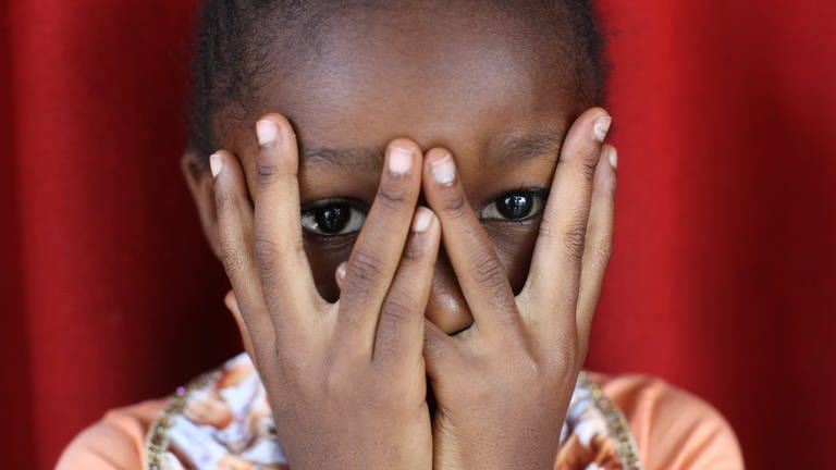 Afrikanisches Mädchen hält sich die Hände vors Gesicht: Sexualisierte Gewalt bleibt eine Kriegswaffe. Überlebende Frauen in Bosnien oder Ruanda leiden bis heute unter Ausgrenzung – so wie die Kinder aus den Vergewaltigungen.