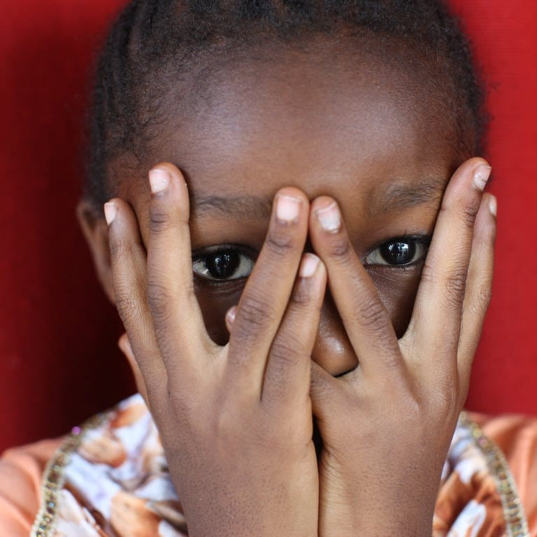 Afrikanisches Mädchen hält sich die Hände vors Gesicht: Sexualisierte Gewalt bleibt eine Kriegswaffe. Überlebende Frauen in Bosnien oder Ruanda leiden bis heute unter Ausgrenzung – so wie die Kinder aus den Vergewaltigungen.