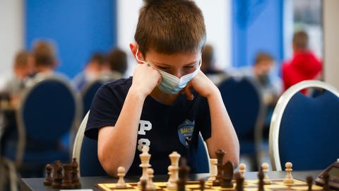 Schachspielender Junge sitzt vor dem Spielbrett.