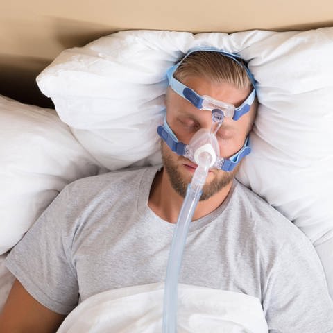 Mann mit Schlafapnoe und CPAP-Gerät: Menschen mit regelmäßigen Atemaussetzern sind häufig abgeschlagen und unkonzentriert (Foto: IMAGO, IMAGO / Panthermedia)