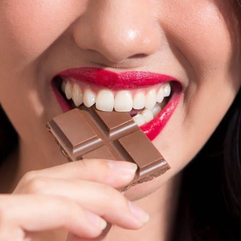 Eine Nahaufnahme von einer Frau, die in ein Stück Schokolade beißt.