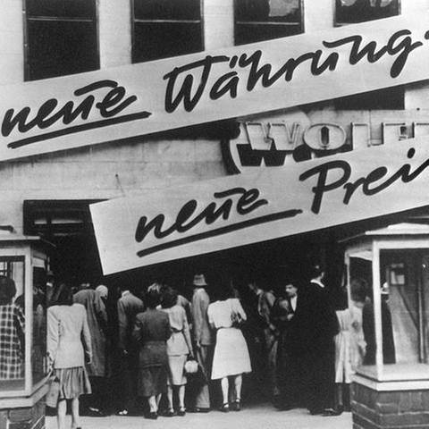 Kundenandrang vor einem Geschäft, das nach der Währungsreform 1948 Schilder mit der Aufschrift "Neue Währung... neue Preise!" an der Hausfassade angebracht hat.