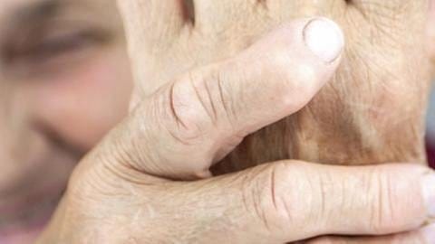Eine ältere Frau greift sich mit schmerzerfülltem Gesicht an ihr Handgelenk.