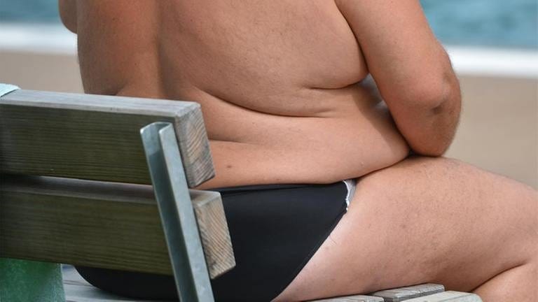 Ein übergewichtiger Mann sitzt auf einer Bank am Strand