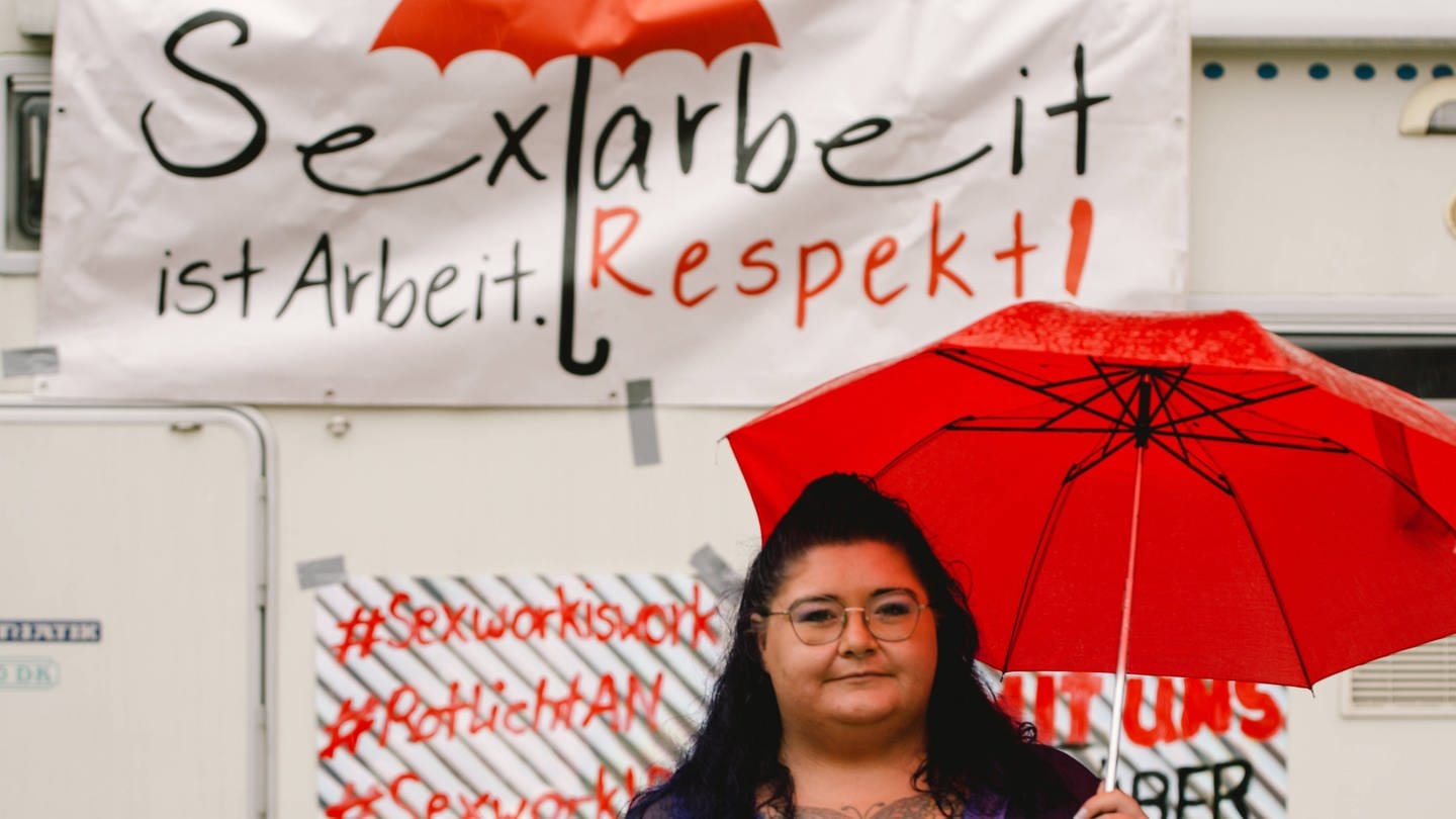 Eine Sexarbeiterin mit rotem Regenschirm in der Hand demonstriet am 22. Juni 2021 vor dem Kölner Dom vor einem Schild mit der Aufschrift: 