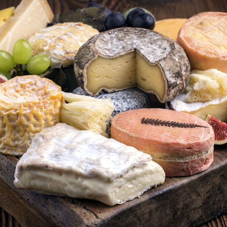 Verschiedene Käsesorten auf einem Holzbrett: Viele Leute schneiden die Rinde beim Käse weg, das wäre aber in den meisten Fällen zumindest aus gesundheitlichen Gründen nicht nötig.