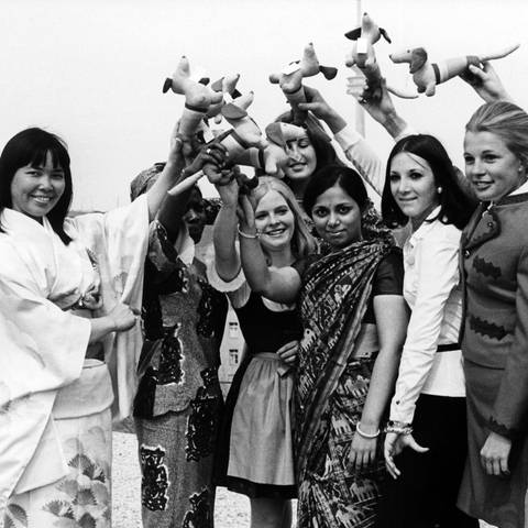 Bereits im April 1971 stellten sich die ersten Hostessen für die Olympischen Spiele 1972 in München vor. Die jungen Frauen aus Japan, Ghana, Indien und Brasilien präsentierten sich mit deutschen Kolleginnen auf dem Oberwiesenfeld und winkten mit dem Maskottchen der Spiele, dem Olympia-Dackel Waldi.  (Foto: picture-alliance / Reportdienste, picture alliance | Lothar Parschauer)