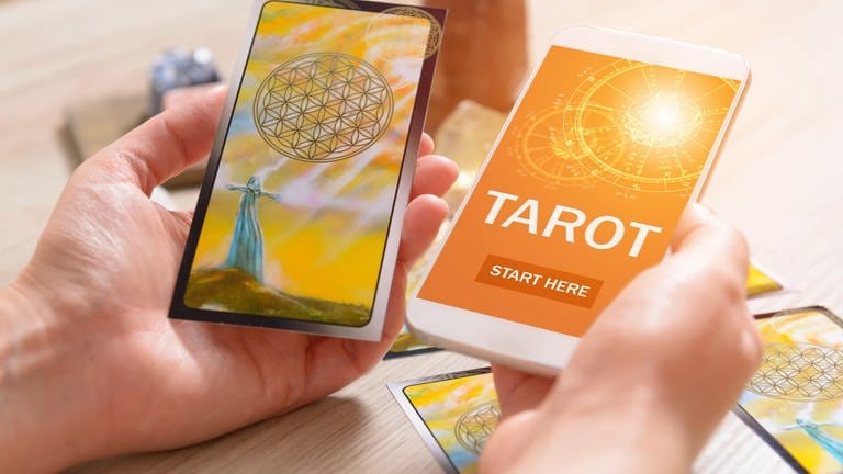 Tarotkarten und Smartphone mit Wahrsage-App: Auf Social Media bieten spirituelle Coaches Instagram-Lives zu Yoga und Meditation an, posten Kacheln zu Selbstliebe und positivem Denken oder legen Tarot-Karten. 